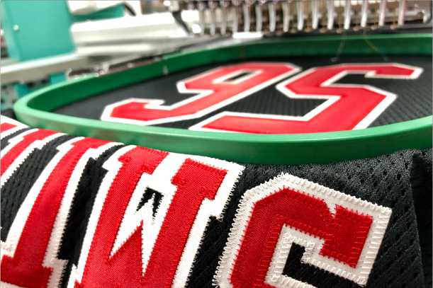 Red and white tackle twill numbers satin-stitched onto black mesh, hooped on the embroidery machine