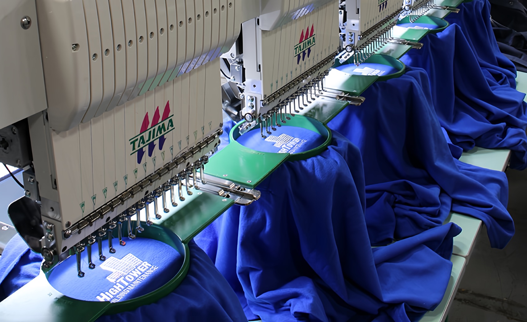 A multi-head embroidery machine stitching logos into hooped blue garments