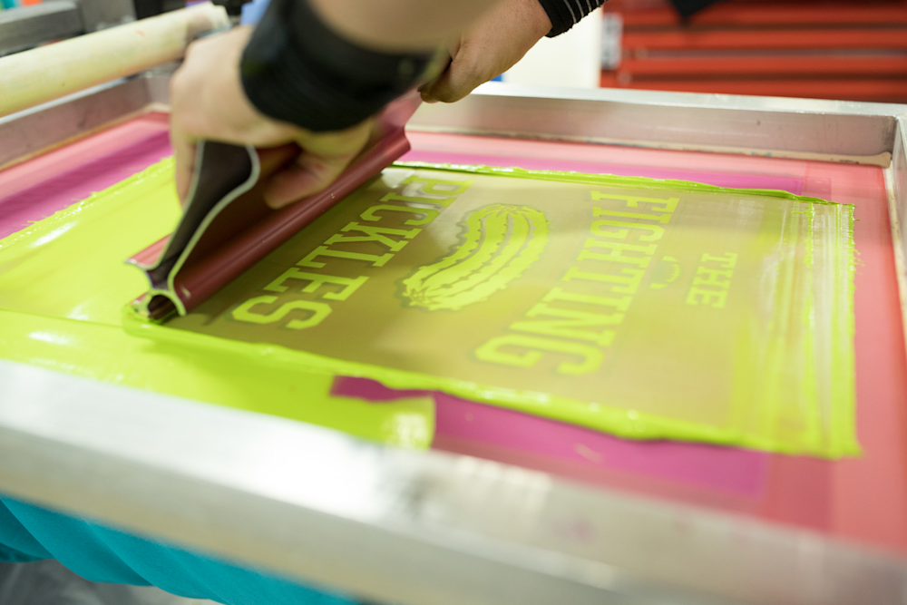 A squeegee pulling neon green plastisol through a taped screen