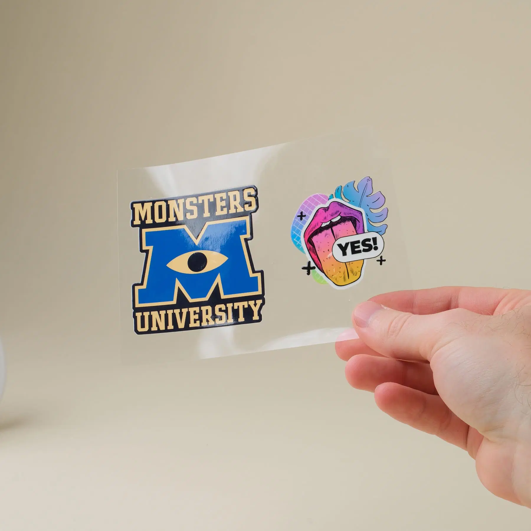A clear UV transfer sheet held up to the light, two full-colour stickers printed on it ready to apply